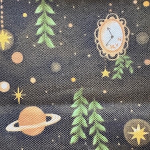 May include: Dark blue fabric with a celestial pattern. The design includes a planet with rings, stars, a clock, and green leaf-like shapes. The background is speckled with small dots.