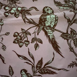 May include: A light pink fabric featuring a repeating dark brown print of birds perched on branches, clusters of berries, and small insects. The detailed illustration shows two distinct bird figures, leafy foliage, and various botanical elements.