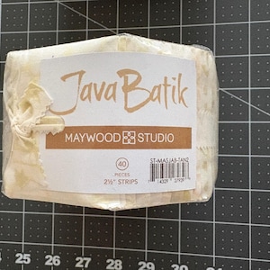 May include: A bundle of 40 tan and cream Java Batik fabric strips by Maywood Studio, wrapped in clear plastic. The label displays the text Java Batik, Maywood Studio, 40 pieces, 2 1/2 inch strips, and the product code ST-MASJAB-TAN2.