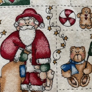 May include: A red and white Santa Claus holding a bag of gifts and a teddy bear. The background is a cream colored fabric with a repeating pattern of stars, candy canes, gingerbread men, and hearts.