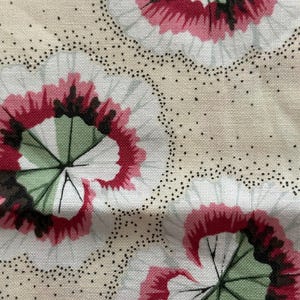 May include: Close-up of a fabric with a repeating floral pattern. The design features large, stylized flowers with red petals and green centers, set against a cream-colored background. Small black dots outline the floral shapes.