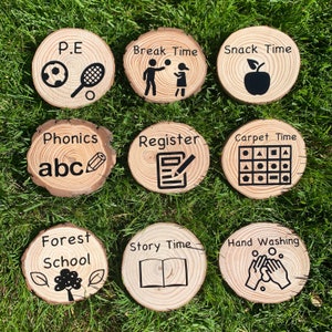 May include: Nine wooden circle signs with black text and icons. The signs include: P.E., Break Time, Snack Time, Phonics, Register, Carpet Time, Forest School, Story Time, and Hand Washing.