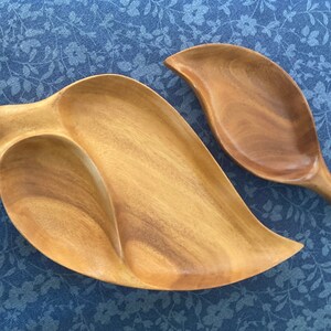 Könnte beinhalten: Zwei hölzerne Servierplatten in Blattform. Die größere Platte hat drei Abschnitte und die kleinere Platte ist ein einziger Abschnitt. Beide Platten sind aus hellbraunem Holz.