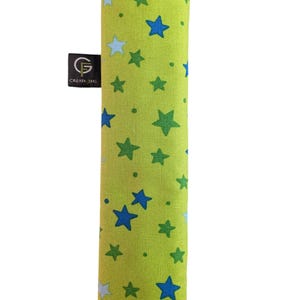 Puede incluir: Una funda de tela rectangular en color verde lima con un patr&oacute;n disperso de estrellas azules, verde oscuro y azul claro. Una peque&ntilde;a etiqueta de tela negra en el lateral muestra un logotipo blanco con el texto G CREATIONS en un dise&ntilde;o circular.