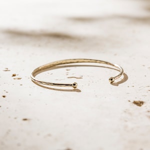May include: A simple gold bangle bracelet with hammered texture and rounded ends.