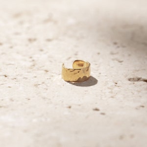 May include: Gold hammered ear cuff. The cuff is a simple, curved band with a hammered texture.