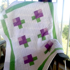 Könnte beinhalten: Eine weiße Steppdecke mit grünem Rand und lila und grünen Blumendesigns.