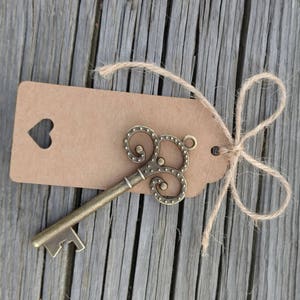 May include: A vintage-style key bottle opener with a brown paper tag tied with twine. The tag has a heart-shaped cutout.