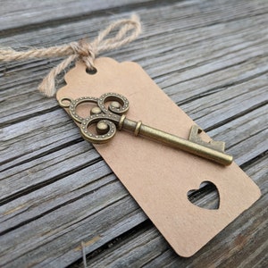 May include: A vintage-style bottle opener shaped like a key with a brown paper tag tied with twine. The tag has a heart-shaped cutout.