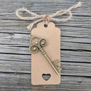May include: A brown paper tag with a heart-shaped cutout and a decorative key-shaped bottle opener attached. The tag is tied with twine.