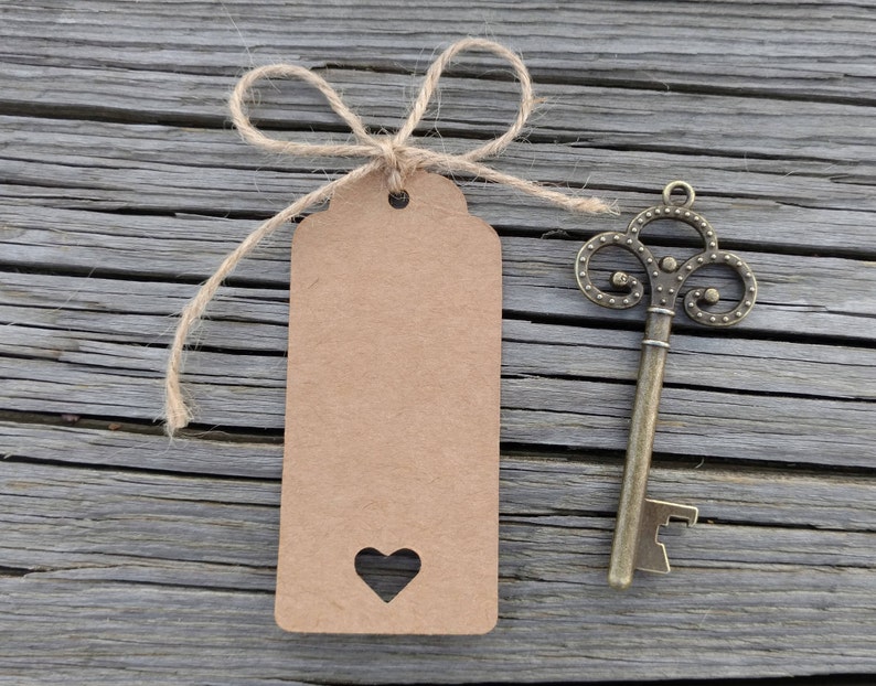 May include: A brown paper tag with a heart cut out and a twine bow tied around it. A vintage key with a bottle opener attached is on a weathered wooden surface.