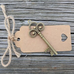 May include: A vintage-style key bottle opener with a brown paper tag tied with twine. The tag has a heart-shaped cutout.