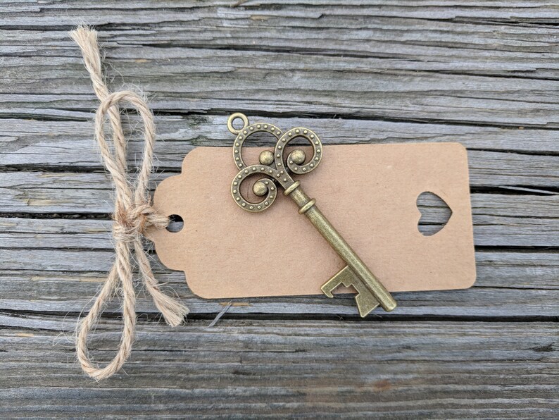 May include: A vintage-style key bottle opener with a brown paper tag tied with twine. The tag has a heart-shaped cutout.