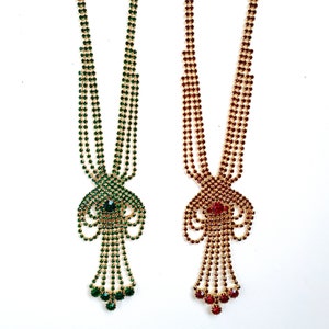 Könnte beinhalten: Zwei goldfarbene Halsketten mit einem baumelnden Design. Eine Halskette hat grüne Strasssteine und die andere rote Strasssteine.