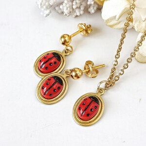 May include: A gold necklace and earrings set featuring a red ladybug charm. The necklace has a delicate chain and the earrings are stud style.