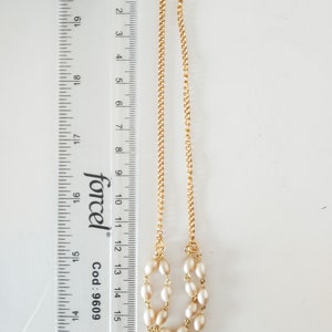 May include: A gold chain necklace with a double strand of cream-colored oval pearls. The necklace is 14 inches long and has a lobster clasp.
