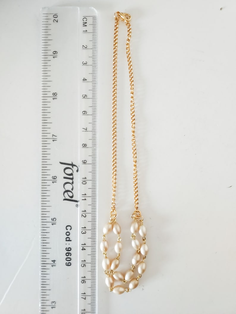 May include: A gold chain necklace with a double strand of cream-colored oval pearls. The necklace is 14 inches long and has a lobster clasp.
