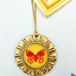 May include: Gold necklace with a round pendant featuring a red and orange butterfly inside a gold frame. The pendant has a yellow background.