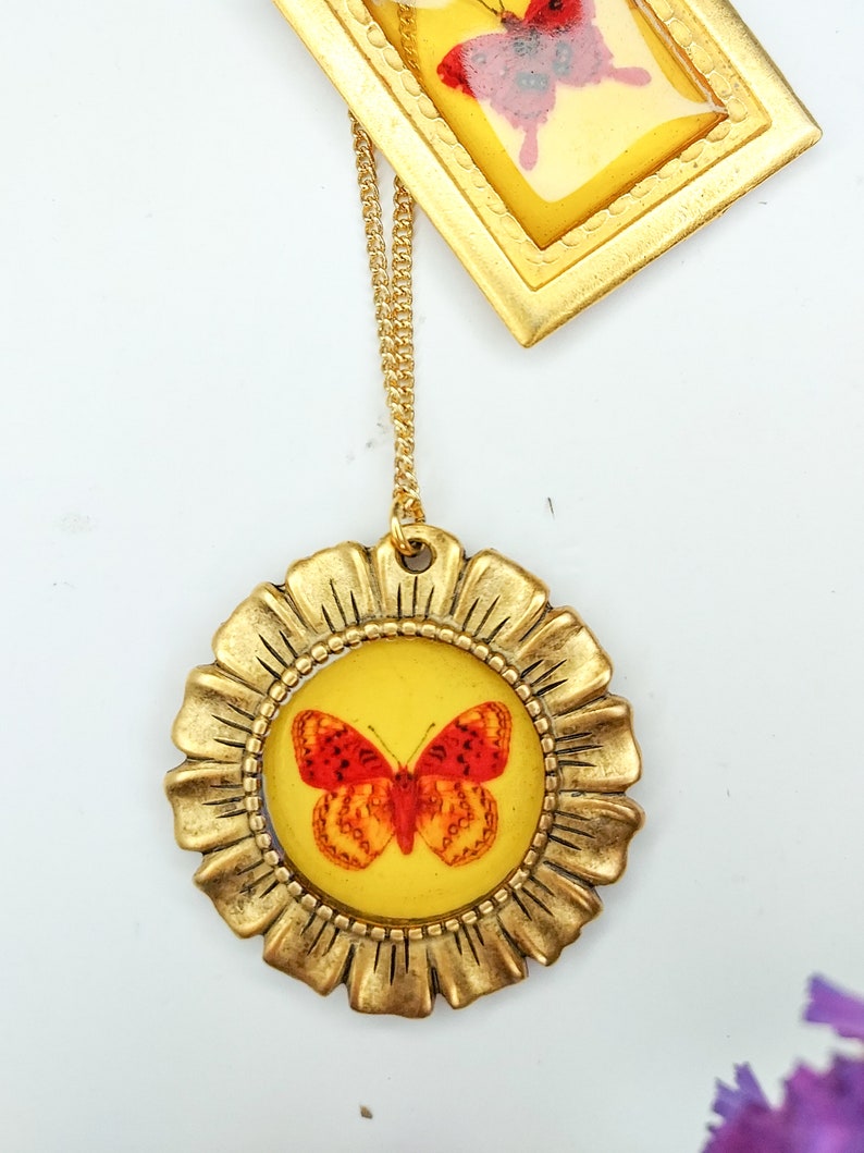 May include: Gold necklace with a round pendant featuring a red and orange butterfly inside a gold frame. The pendant has a yellow background.