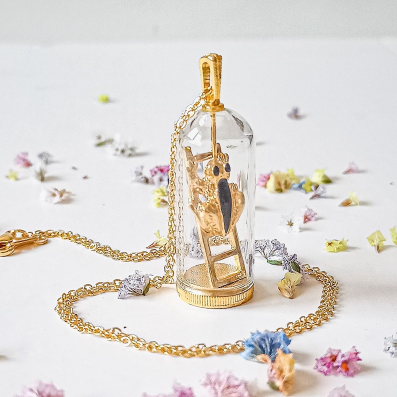 May include: A gold necklace with a glass pendant featuring a small golden figure climbing a ladder. The pendant is clear and the figure is visible inside.