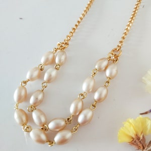 May include: A gold chain necklace with two rows of oval-shaped cream-colored pearls.
