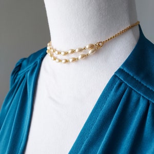 May include: A gold chain necklace with two rows of oval-shaped faux pearls. The necklace is on a white mannequin.