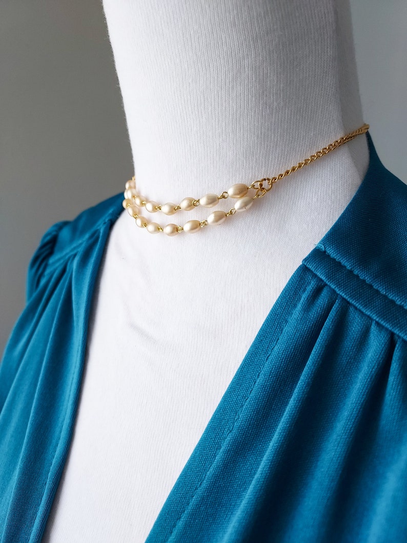 May include: A gold chain necklace with two rows of oval-shaped faux pearls. The necklace is on a white mannequin.