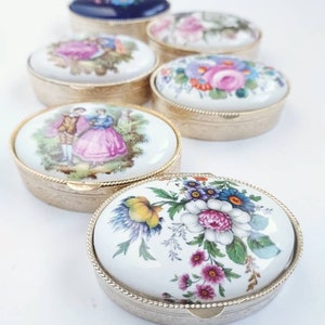 May include: Six oval porcelain trinket boxes with gold trim. The boxes are decorated with floral and romantic scenes.