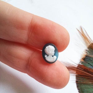 Op de afbeelding: Een witte cameo met het profiel van een vrouw, ingelijst in een donkerblauw ovaalvormig frame.