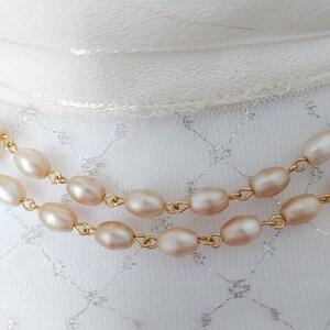 May include: Two strands of a pearl necklace with gold chain links. The pearls are a pale pink color and are oval shaped.