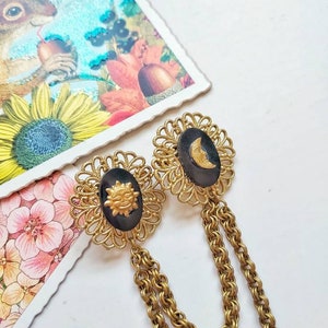 A matte old gold tone collar chain made with unused vintage parts:  two decorative circular filigrees featuring a black shell cabochon with a brass miniature overnthem each of them: a sun and a moon, both with faces. 
They have two sturdy chains linked to each filigree.