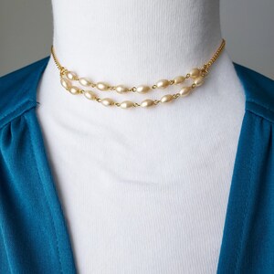 May include: A gold chain necklace with two rows of oval-shaped faux pearls. The necklace is on a white mannequin.