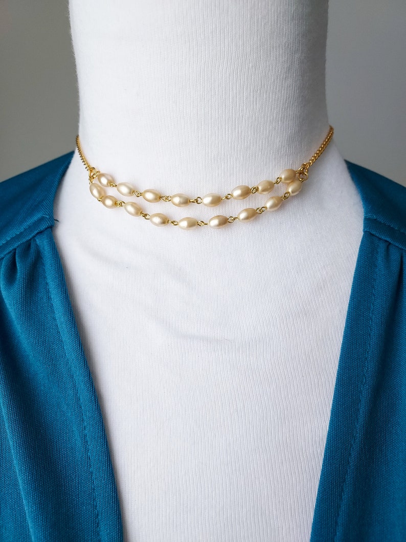 May include: A gold chain necklace with two rows of oval-shaped faux pearls. The necklace is on a white mannequin.