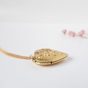Op de afbeelding: Een gouden ketting met een hartvormige hanger met een bloemenmotief. Het medaillon is open en de ketting is zichtbaar.