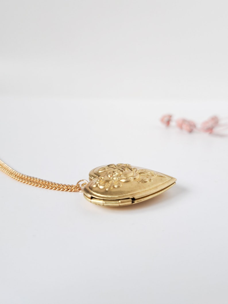 Op de afbeelding: Een gouden ketting met een hartvormige hanger met een bloemenmotief. Het medaillon is open en de ketting is zichtbaar.