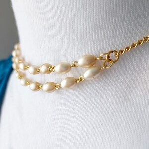 May include: A gold chain necklace with two strands of oval-shaped faux pearls.