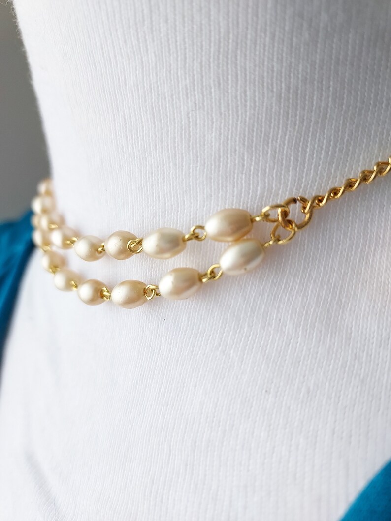 May include: A gold chain necklace with two strands of oval-shaped faux pearls.