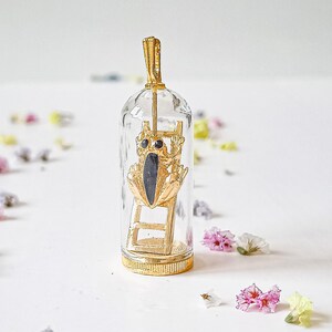 May include: A gold pendant featuring a small frog figurine climbing a ladder inside a glass dome. The frog has black eyes and a black body.