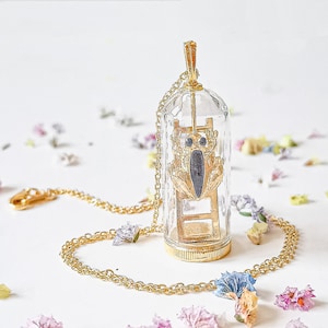 May include: A gold necklace with a glass pendant containing a gold beetle climbing a ladder. The pendant is suspended from a gold chain.