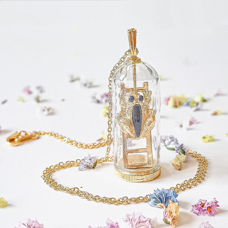 May include: A gold necklace with a glass pendant containing a gold beetle climbing a ladder. The pendant is suspended from a gold chain.