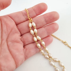 May include: A gold chain necklace with white oval-shaped beads. The necklace is on a hand.
