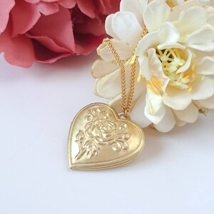Op de afbeelding: Een gouden ketting met een hartvormige hanger met een roosontwerp. De hanger hangt aan een delicate gouden ketting.