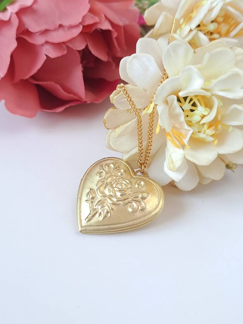 Op de afbeelding: Een gouden ketting met een hartvormige hanger met een roosontwerp. De hanger hangt aan een delicate gouden ketting.