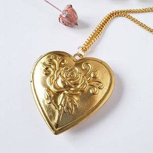 Op de afbeelding: Een gouden ketting met een hartvormige hanger met een roosontwerp. De hanger heeft een gedetailleerd bloemmotief en een fijne ketting.