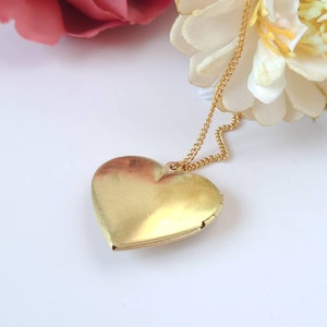 Op de afbeelding: Een gouden hartvormige hanger aan een gouden ketting. De hanger is gesloten en de ketting hangt naar beneden.