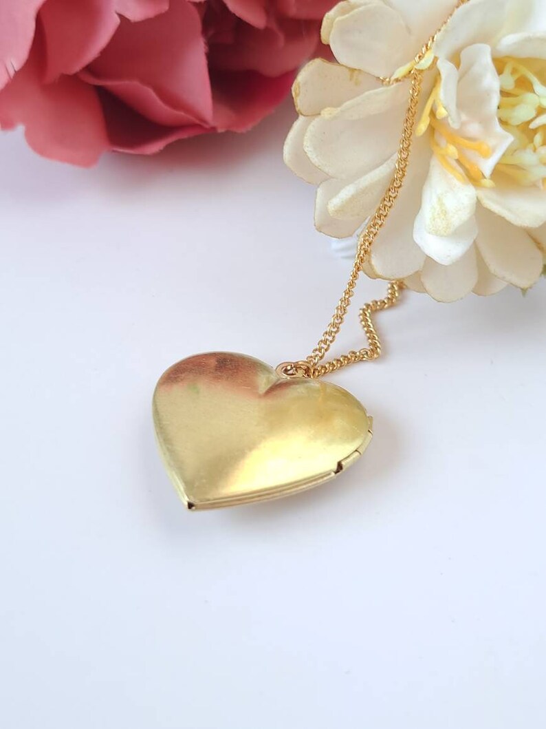 Op de afbeelding: Een gouden hartvormige hanger aan een gouden ketting. De hanger is gesloten en de ketting hangt naar beneden.