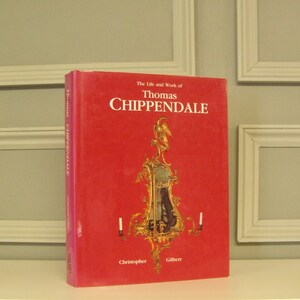 May include: A red hardback book titled "The Life and Work of Thomas Chippendale" by Christopher Gilbert. The book cover features a gold illustration of a decorative mirror with candlesticks.