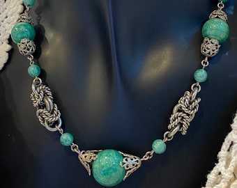Puede incluir: Un collar de cadena de plata con cuentas de jade verde y detalles plateados. El collar presenta una gran cuenta de jade redonda en el centro.