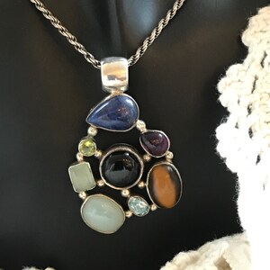 May include: A silver necklace with a pendant featuring a cluster of colorful gemstones, including lapis lazuli, amethyst, tiger's eye, and green stones.