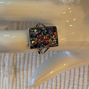 May include: A square-shaped ring with a colorful mosaic design set in a silver-toned metal frame.